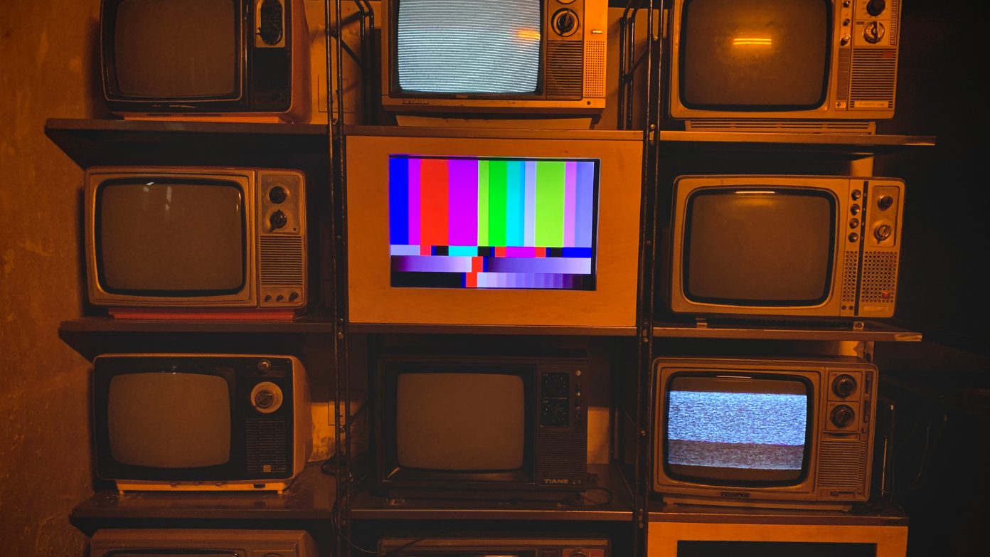 A wall of vintage TVs, one showing color bars