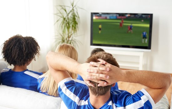 Friends in team jerseys watching a soccer game on a wall-mounted TV